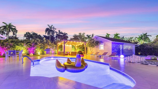 A swimming pool with a swan-shaped inflatable float, lounge chairs, and a covered seating area with string lights. - Luxury Villa Serena Heated Pool 15 min to Beach (Miami)
