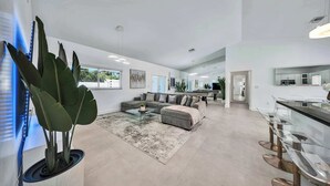 A modern living room with a sectional sofa, a glass coffee table, and a large potted plant. - Luxury Villa Serena Heated Pool 15 min to Beach (Miami)