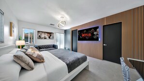A modern bedroom with a bed, a TV mounted on the wall, and a wooden panel design. - Luxury Villa Serena Heated Pool 15 min to Beach (Miami)