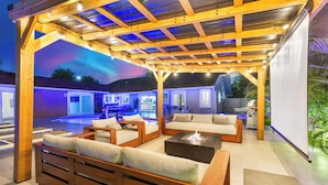 An outdoor patio with wooden furniture, a fire pit, and a pool area in the background. - Luxury Villa Serena Heated Pool 15 min to Beach (Miami)