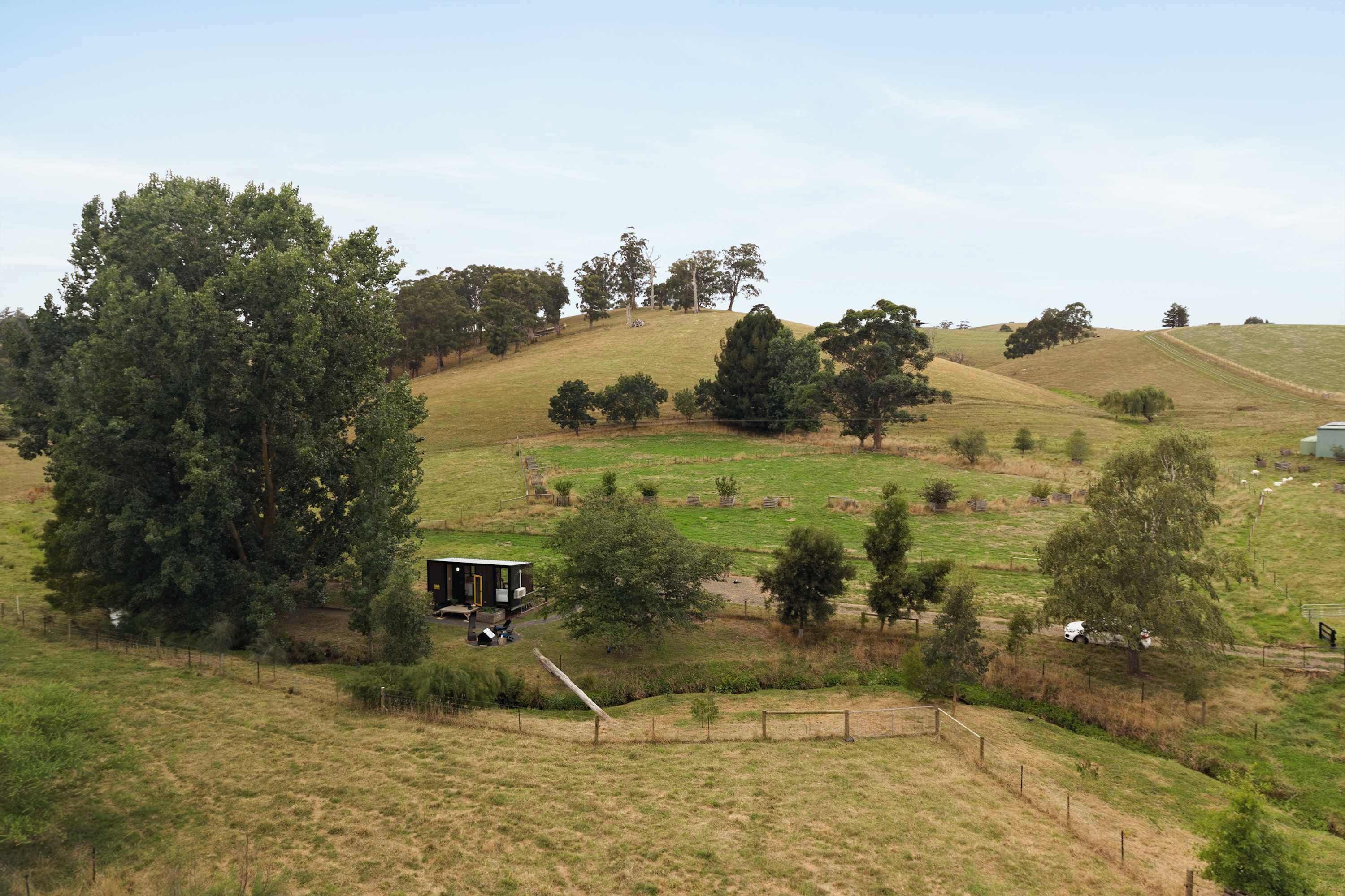 Paisaje rural con colinas ondulantes, una propiedad cercada y un edificio pequeño con porche.