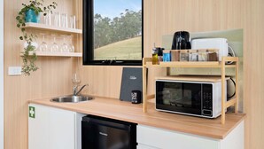 A compact kitchen with a sink, a microwave, and a compact dishwasher. There are shelves with glassware and a potted plant.