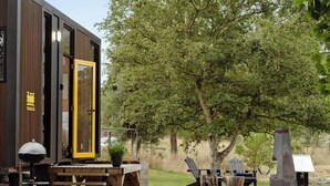 A wooden cabin with a yellow door, a barbecue grill, and outdoor seating.