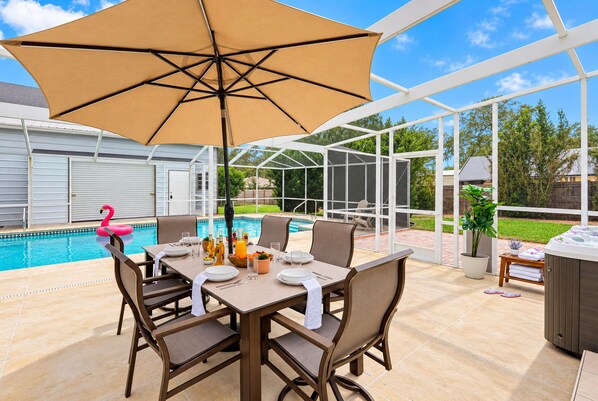 An outdoor patio with a table set for dining, a pool, and a hot tub.