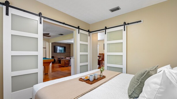 A hotel room with a bed, a breakfast tray, and a sliding door leading to a kitchen area. - Brandon Getaway | 4BR Home w/ Pool & Hot Tub (Brandon)
