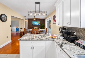 A modern kitchen with a marble island, a coffee bar, and a dining area with a TV. - Brandon Getaway | 4BR Home w/ Pool & Hot Tub (Brandon)