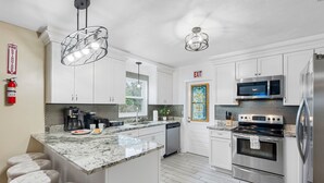 A modern kitchen with white cabinets, stainless steel appliances, and a marble island with bar stools. - Brandon Getaway | 4BR Home w/ Pool & Hot Tub (Brandon)