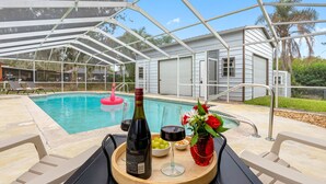 A pool area with a covered seating area, a bottle of wine, a glass, and a bowl of grapes on a tray. - Brandon Getaway | 4BR Home w/ Pool & Hot Tub (Brandon)