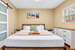 A bedroom with a large bed, bedside tables, a window with blinds, and three wall-mounted pictures. - Brandon Getaway | 4BR Home w/ Pool & Hot Tub (Brandon)