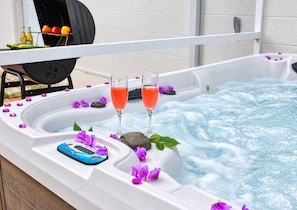 Een jacuzzi met twee glazen roze drank, omringd door paarse bloemen en een smartphone op de rand.