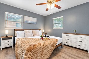 A bedroom with a bed, bedside tables, a dresser, a ceiling fan, and artwork on the walls.