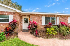 A brick building with a white door, a garage, and a landscaped front yard with various plants.