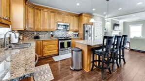 A modern kitchen with wooden cabinets, granite countertops, stainless steel appliances, and a bar area with stools.
