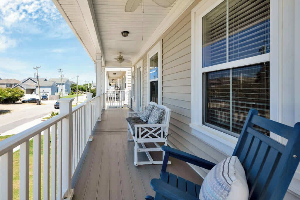 A covered porch with a white railing, a blue bench, and a white rocking chair.
