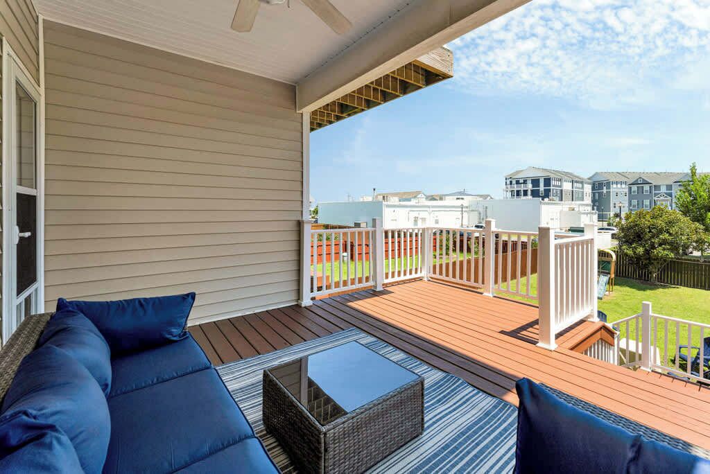 A covered outdoor deck with a sofa and a coffee table, overlooking a residential area.