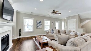 A spacious living room with a fireplace, a large sofa, a coffee table, and a ceiling fan.