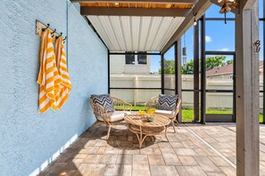 Ein überdachter Patio-Bereich mit Korbmöbeln, einem Tisch mit einer Obstschale und einer blauen Wand mit gestreiften Handtüchern.