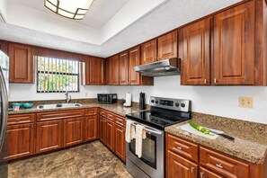 Una cocina con armarios de madera, una estufa de acero inoxidable, un microondas y encimeras de granito.