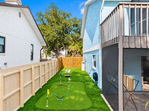 A residential backyard with a wooden fence, a lawn, and a tennis court.