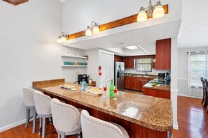 Una cocina moderna con encimeras de granito, armarios de madera y una zona de bar con taburetes.