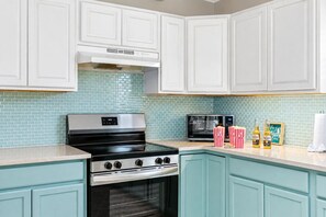 Una cocina con armarios blancos, estufa, horno, microondas y salpicadero de azulejos.