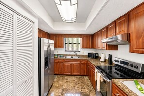 A modern kitchen with wooden cabinets, stainless steel appliances, and a granite countertop. - The Cardinal Cove | Spacious Palm Harbor Retreat (Palm Harbor)