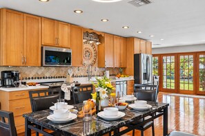 A modern kitchen with wooden cabinets, a stainless steel refrigerator, and a dining area with a marble table set for a meal.