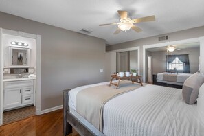 Une chambre à coucher avec un lit, une coiffeuse avec un miroir et un ventilateur de plafond.