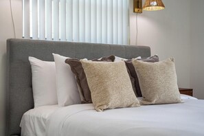 A bed with white bedding and a grey headboard.