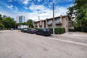 A residential street with a row of parked cars, a stop sign, and a building with balconies.