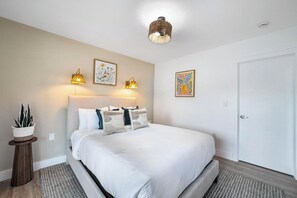 Quarto bem arrumado com uma cama grande, duas luminárias na parede e duas obras de arte com flores emolduradas.