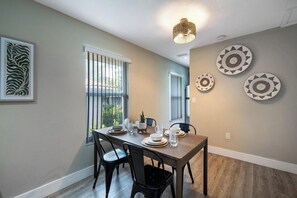 A dining area with a table set for four, a window with vertical blinds, and three decorative plates on the wall.