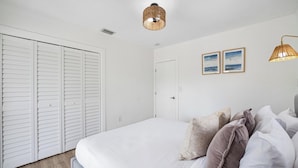 A bedroom with a large bed, white walls, a white door, and two wall-mounted lights.