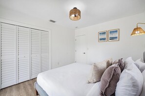 A bedroom with a large bed, white walls, a white door, and two wall-mounted lights.