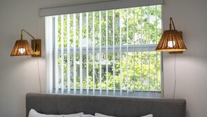 A bedroom with a large window, a grey sofa, and two wall-mounted lamps.