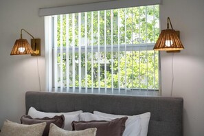 Quarto com uma janela grande, um sofá cinzento e duas luminárias fixadas na parede.