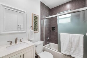 A modern bathroom with a white sink, vanity, and toilet. There is a glass-enclosed shower area with a bathtub.