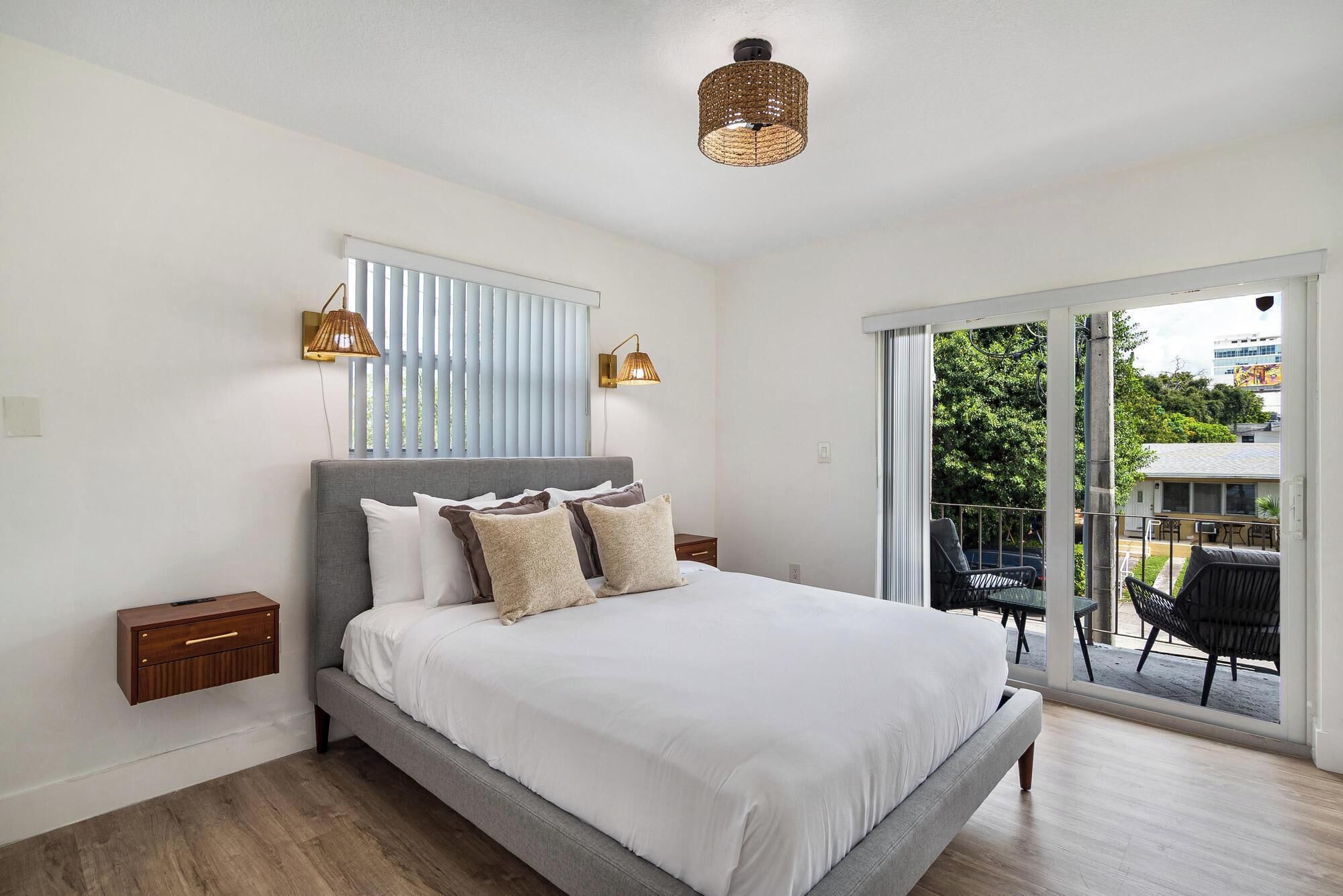 Une chambre à coucher comprenant un lit, deux tables de chevet, une fenêtre avec des stores et une vue sur l’extérieur.