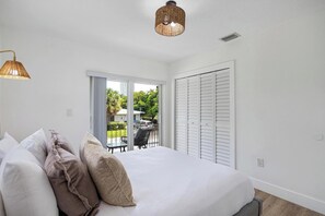 A bedroom with a bed, pillows, a balcony with a view, and a ceiling light.