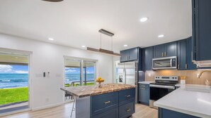 A modern kitchen with dark cabinets, a wooden island, and a view of the ocean.