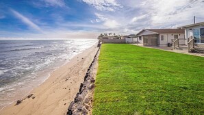 A beachfront property with a grassy lawn, a wooden deck, and a view of the ocean.
