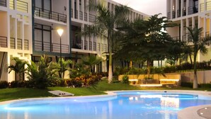 Une piscine entourée d’un jardin bien entretenu, agrémenté de palmiers, et un bâtiment moderne doté de balcons.