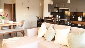 Un salon moderne avec un canapé, une table à manger et des chaises. On y trouve également un coin cuisine avec des placards et une horloge au mur.