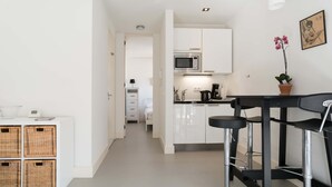 A modern kitchen with white cabinets, a microwave, and a coffee maker. There is a small dining area with a black bar stool and a potted orchid. - Laurier Apartment - in the Jordaan (Amsterdam)