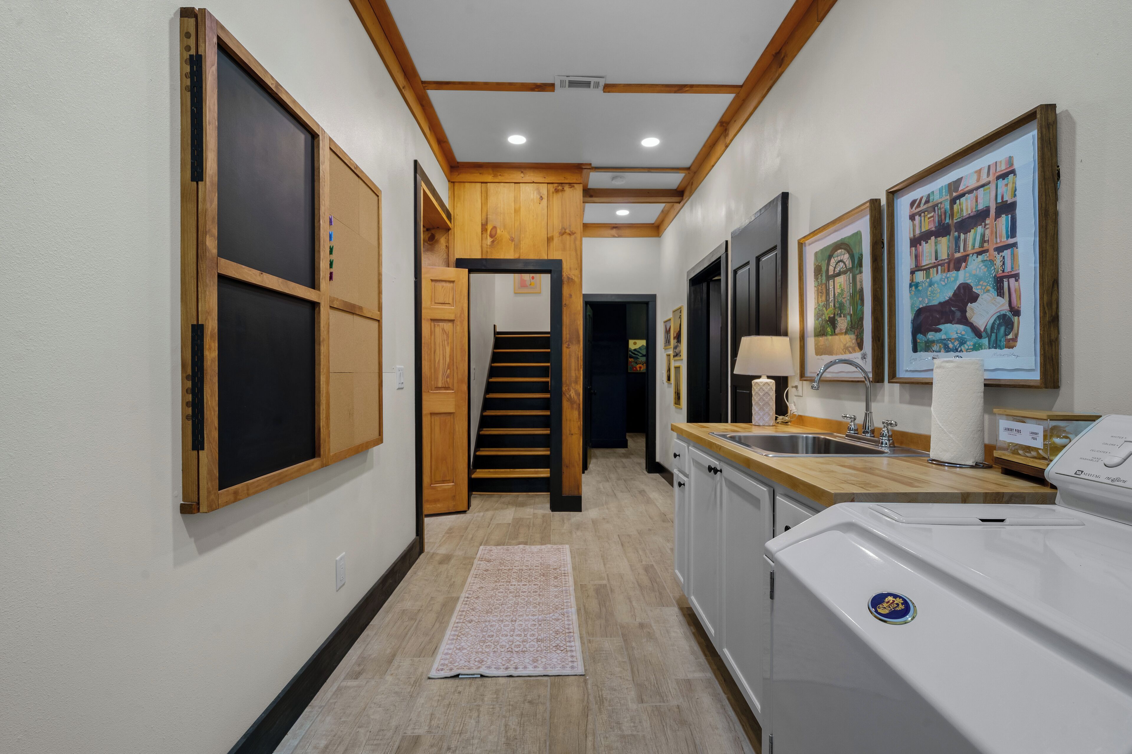 A narrow hallway with wooden walls and a tiled floor, leading to a staircase and a kitchen area with a washing machine.