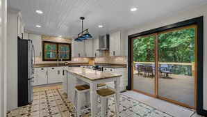 A modern kitchen with white cabinetry, a large island with stools, and a sliding glass door leading to an outdoor patio.
