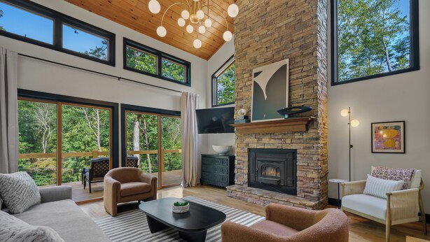 A spacious living room with a fireplace, large windows, and a high ceiling.