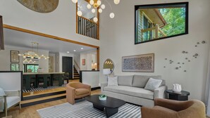 A spacious living area with a high ceiling, a staircase, and a view of the outdoors.