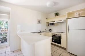 Une cuisine avec des meubles blancs, un four à micro-ondes, un réfrigérateur et une fenêtre donnant sur un paysage verdoyant.
