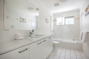 A modern bathroom with a large mirror, two sinks, a toilet, and a bathtub.